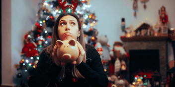 woman holiding empty piggy bank in front of a Christmas tree
