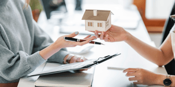 woman's hand with small house reaching out to another woman