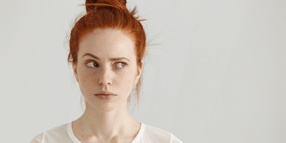 A red-headed woman with a messy bun looking to the left while raising an eyebrow