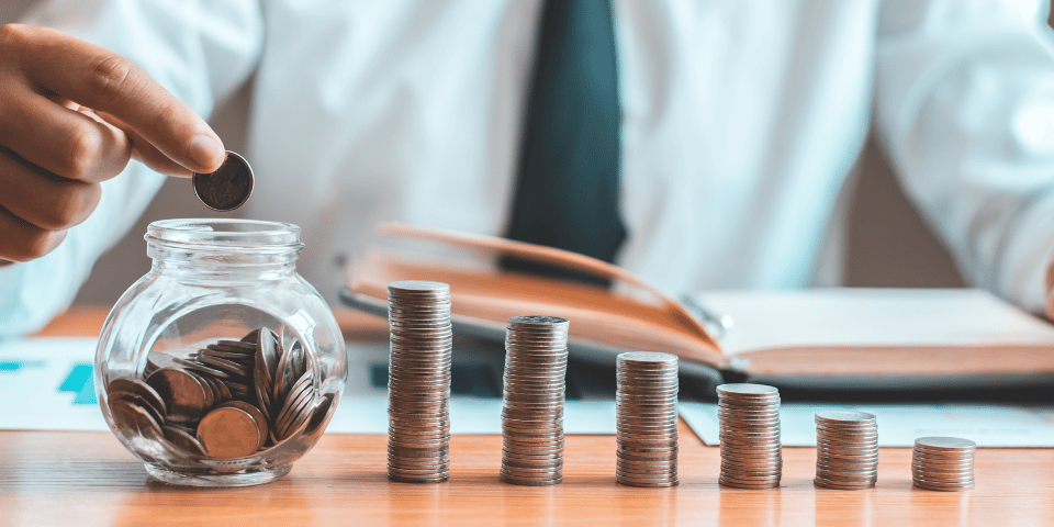 Close up view of a man dressed in a shirt and tie, placing stacked coins into a glass jar. 