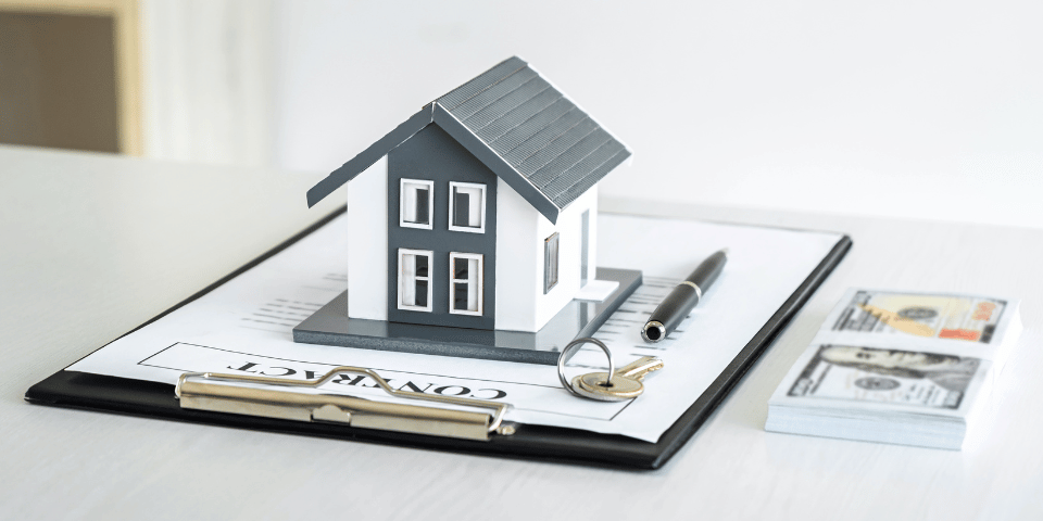 Model house sitting on a clipboard with keys and a pen