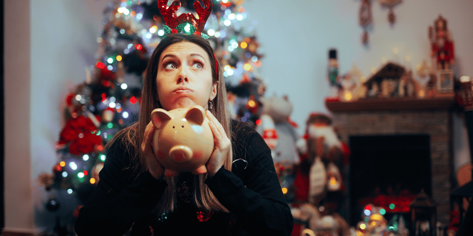 woman holiding empty piggy bank in front of a Christmas tree