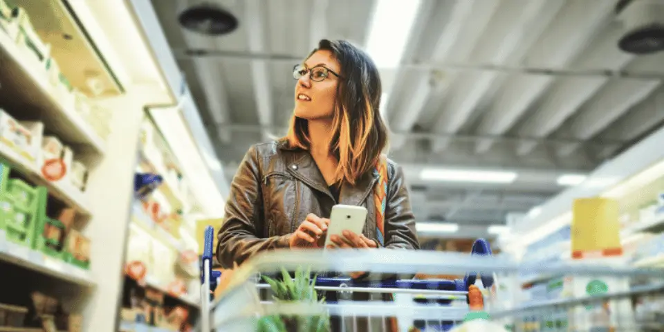 Young woman grocery shopping with her phone in hand