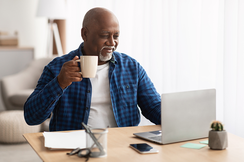 man sits at his computer with a mug of coffee in his hand